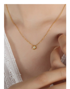 Close-up of a minimalist gold necklace with a round zircon pendant on a woman's collarbone