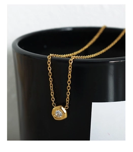 Close-up of golden necklace with hexagonal nut pendant and cubic zirconia on black cup