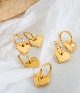 Dettaglio di tre paia di orecchini a cerchio con cuore in oro 18K su carta bianca