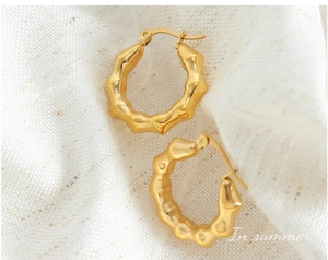 Detailed view of gold C-shaped wavy hoop earrings on a white fabric background
