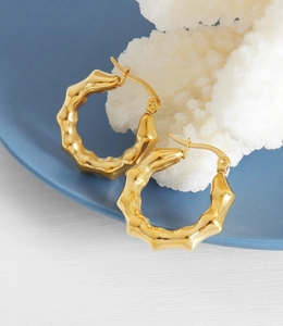 Macro detail of gold-plated bamboo texture C-shaped hoop earrings on coral stone