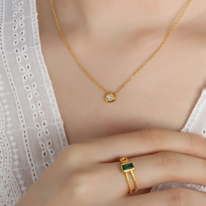 Elegant gold necklace with solitaire pendant and emerald ring on lace outfit