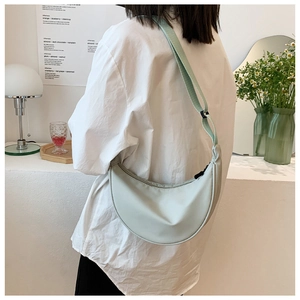 Light green nylon crescent bag worn crossbody, showing its adjustable strap and smooth texture