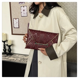 Detail of dark red snakeskin envelope clutch with gold V-trim and metal buckle