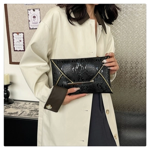 Detail of elegant black snakeskin textured clutch with gold metal trim held by model