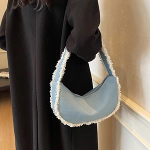 Sac hobo en jean bleu clair avec franges blanches porté avec un long manteau noir