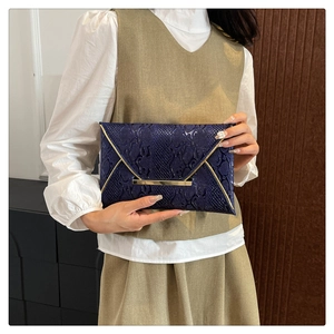Detailed view of dark blue snakeskin embossed texture with gold metal trim on envelope clutch
