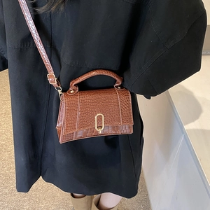 Sac à bandoulière marron motif crocodile avec fermoir doré porté par un mannequin en manteau