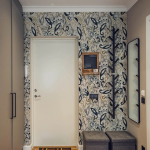 Detail view of a black tree-shaped metal wall coat rack against vintage pattern wallpaper