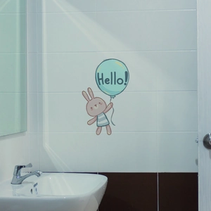 Detail of a rabbit and green balloon wall sticker on a white tile bathroom wall