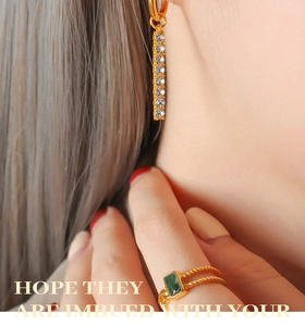 Detail of 18K gold earrings with zircons and a green gemstone ring on a model