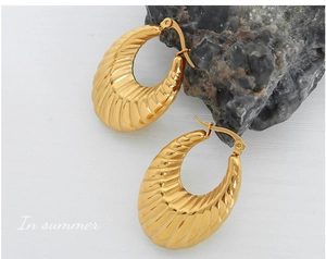 Détail de boucles d'oreilles en U dorées avec texture côtelée sur fond de pierre