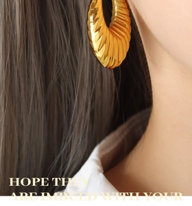 Gros plan de boucles d'oreilles en U dorées avec texture plissée radiale sur mannequin