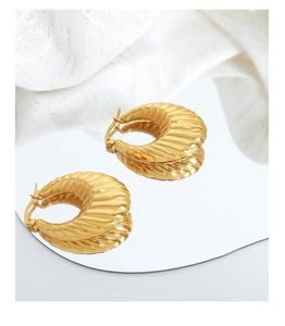Gros plan de boucles d'oreilles croissant dorées en U avec reflet sur tissu blanc