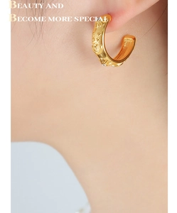 Detailed close-up of gold C-shaped hoop earrings with embossed celestial moon and star patterns