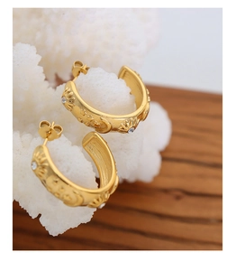 Detail of gold sun and moon relief hoop earrings with crystal accents on coral base