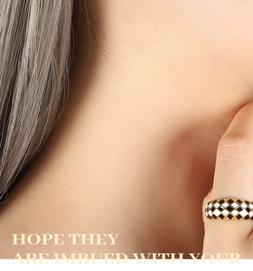 Detailed view of checkered black and white enamel heart ring with gold finish on finger