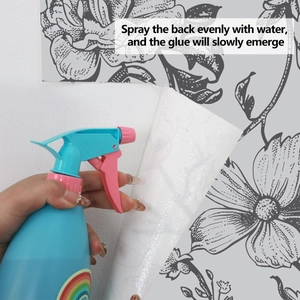 Close-up of spraying water to activate adhesive on floral wallpaper with black line art