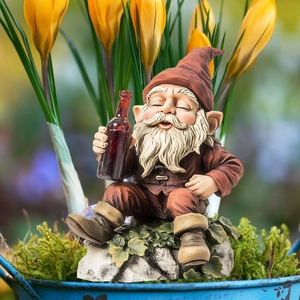 Close-up of a gnome figurine holding a wine bottle on a mossy rock in a lush garden