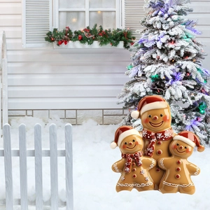 Three gingerbread family figurines with red hats in a snowy Christmas garden setting