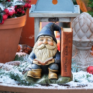 Detail of garden gnome garden stake sitting and reading a book on a snowy background