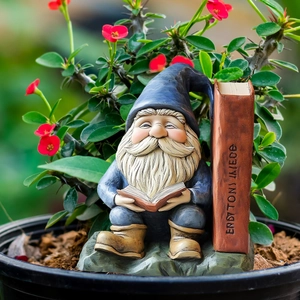 Detail view of a garden gnome reading on a rock by a giant book in a flower pot