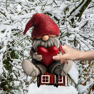 Garden gnome stake decoration sitting on a red house holding a heart on snowy backdrop