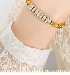 Vue rapprochée d'un bracelet en perles dorées avec anneaux en strass blancs sur dentelle