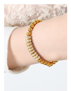 Détail du bracelet à perles dorées avec charmes en strass brillants sur le poignet