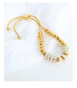 Détail d'un bracelet coulissant doré perlé orné de strass sur un fond texturé blanc