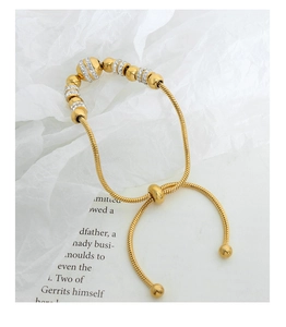 Detailed view of adjustable gold beaded bracelet with crystal pavé charms on a card