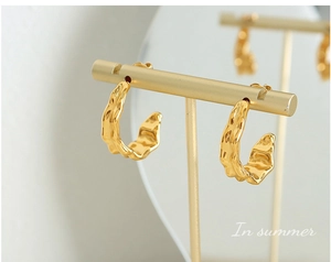 Macro view of gold-plated irregular textured C-shape hoop earrings on a display stand