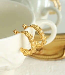 Detail of 18K gold plated C-shape earrings with irregular wavy texture on a white cup