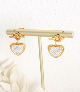 Detail of gold heart earrings with knot design and micro-pave crystals on a display stand