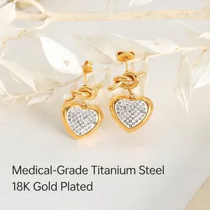 Elegant 18K gold plated heart drop earrings with shimmering crystals on a white plant