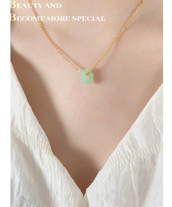 Détail d'un pendentif fleur en jade vert clair sur une chaîne dorée au cou