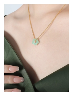 Détail d'un pendentif fleur en jade vert clair sur une chaîne dorée portée par un modèle
