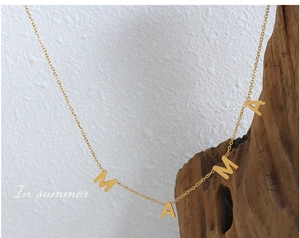 Détail du collier pendentif MAMA doré exposé sur bois rustique avec un éclairage doux