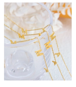 Gros plan du collier MAMA doré suspendu à un verre avec des fleurs décoratives