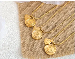 Détail de colliers dorés avec gravure lettre R et pendentif coeur sur tissu en lin