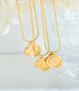 Détail macro du collier en or avec pendentif lettre R et motifs lune et étoile