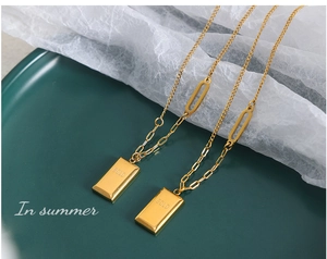 Macro detail of gold-plated rectangular charm necklace with GOLD engraving on dark tray