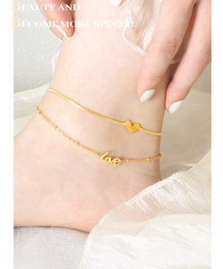 Détail de la chevillère double en or avec pendentifs cœur et love sur la cheville du modèle