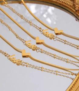 Détail de chaînes de cheville dorées à double rang avec breloque Love et pendentif cœur poli