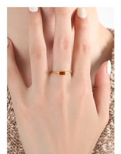 Detail of a thin gold titanium ring with an amber rectangular stone on a finger