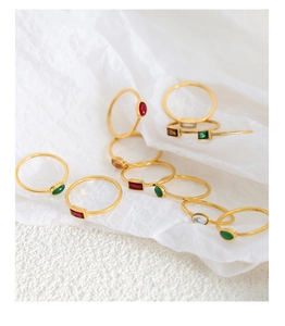 Detail of minimalist gold-plated rings with colorful gemstones on textured paper