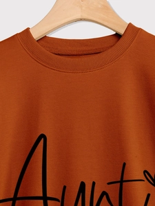 Close-up of ribbed crewneck and black aunt script on orange long sleeve sweatshirt