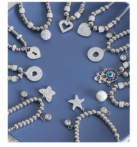 Detailed close-up of silver beaded bracelets with hamsa and heart charms on a blue tray