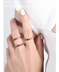 Detail of gold titanium rings with colorful zircon crystals on a model wearing white knit
