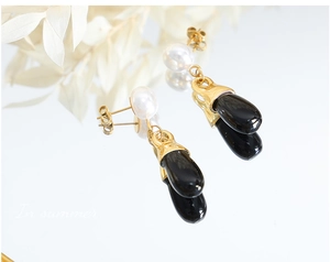 Detail of elegant gold drop earrings featuring white pearls and black teardrop pendants